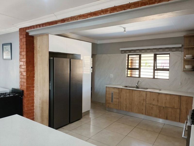 Modern kitchen featuring wood-grain cabinetry, stainless steel sink, tiled flooring, and a distinctive exposed brick architectural feature.