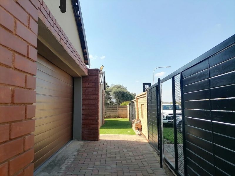 Side access area featuring brick paving, a sectional garage door, and a secure metal gate leading to the front garden.