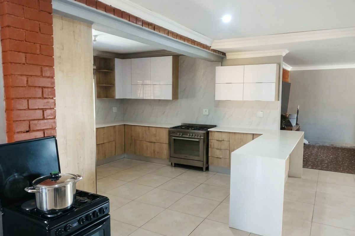 Modern kitchen featuring two-tone cabinetry, stone countertops, a central island, and a gas stove, seamlessly integrated into an open-plan living space.