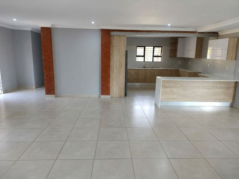 Spacious open-plan living area featuring modern kitchen cabinetry, a central island, tiled flooring, and decorative exposed brick pillars.
