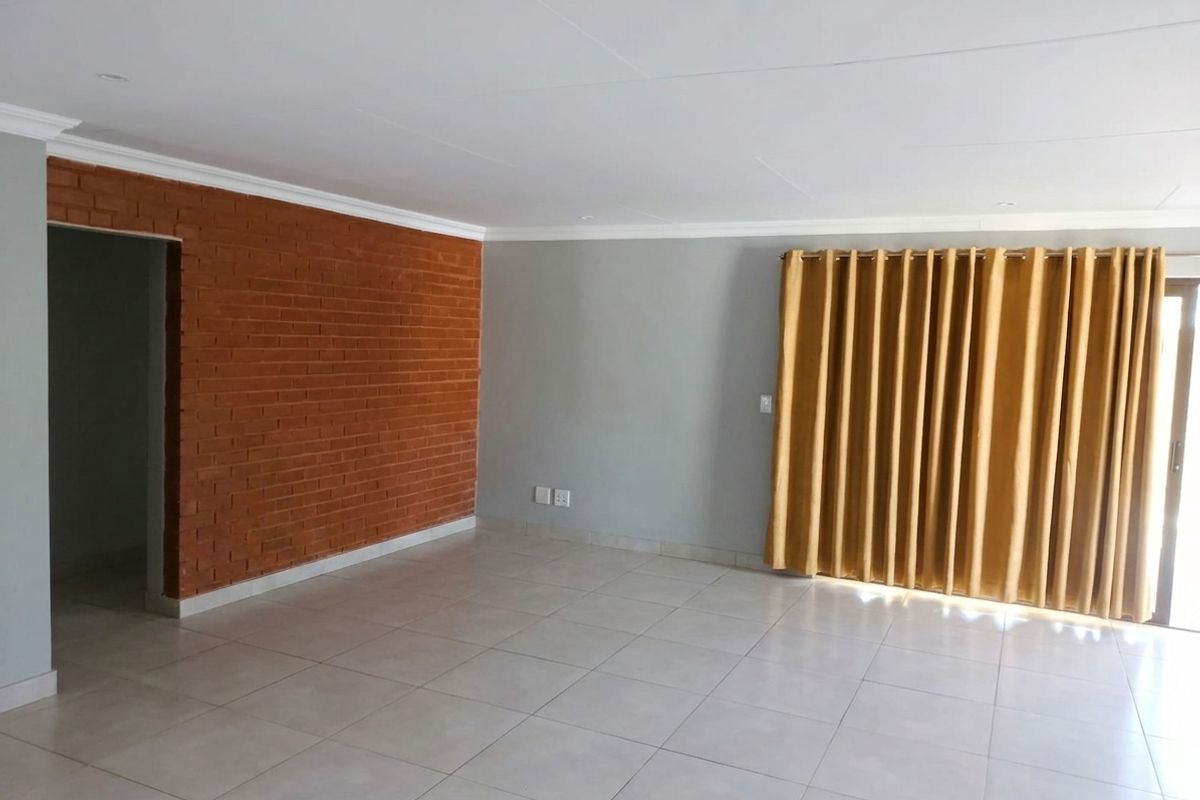 Spacious living area featuring an exposed brick accent wall, neutral ceramic floor tiles, and large sliding doors leading to the exterior.