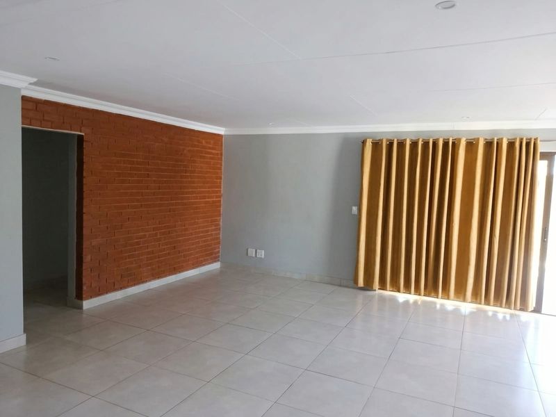 Spacious living area featuring an exposed brick accent wall, neutral ceramic floor tiles, and large sliding doors leading to the exterior.