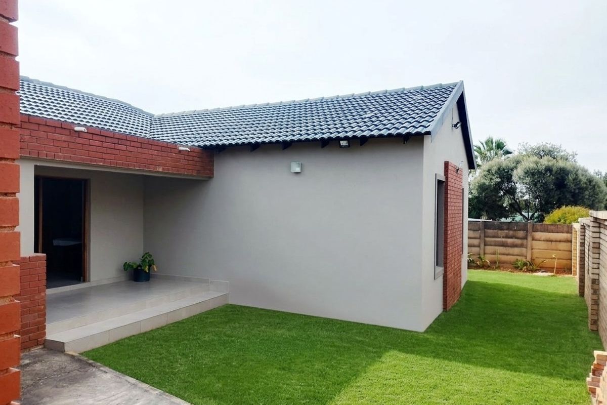 Rear view of the house featuring a covered patio, brick and plastered exterior walls, and a well-maintained lawn.