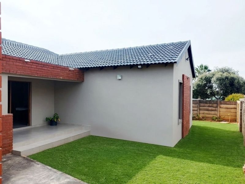 Rear view of the house featuring a covered patio, brick and plastered exterior walls, and a well-maintained lawn.