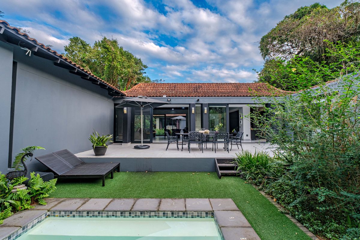 Rear exterior view featuring a tiled patio, swimming pool, and artificial lawn, providing a seamless transition between indoor and outdoor living spaces.