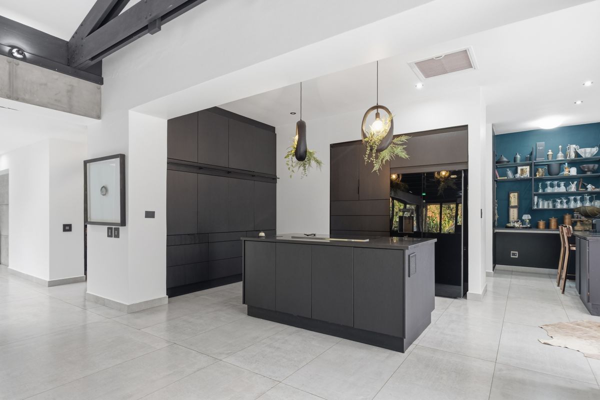 Modern kitchen featuring a central island, sleek dark cabinetry, exposed ceiling beams, and high-quality tiled flooring in an open-plan layout.