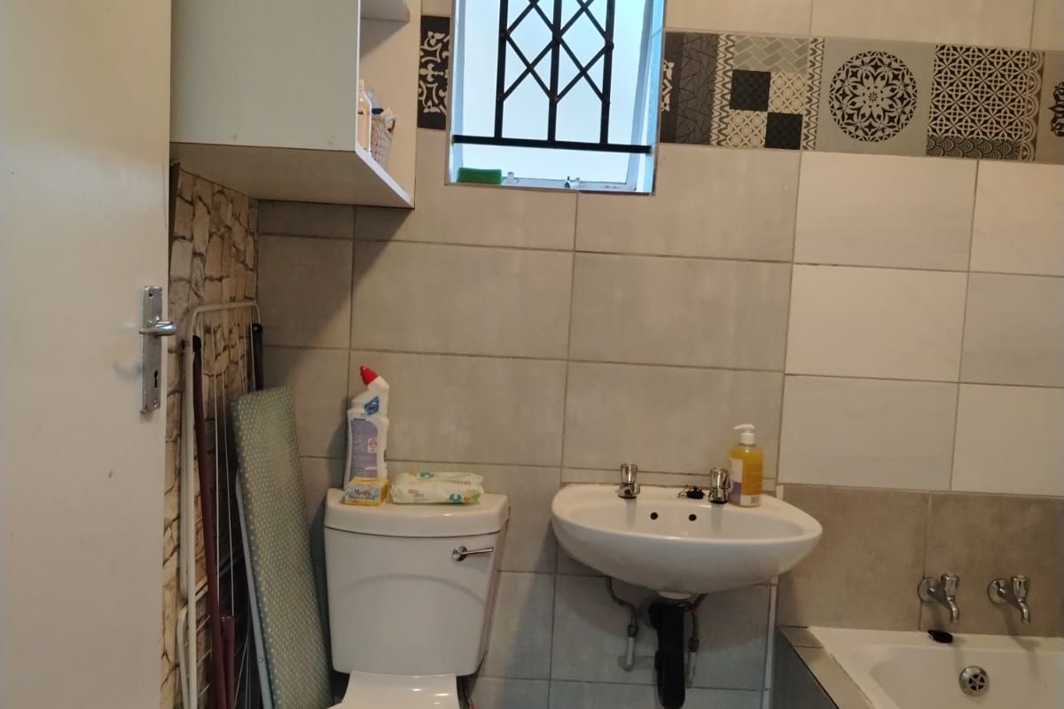 A functional bathroom featuring a bathtub, wall-mounted basin, toilet, and decorative tiled accents with built-in overhead storage shelving.