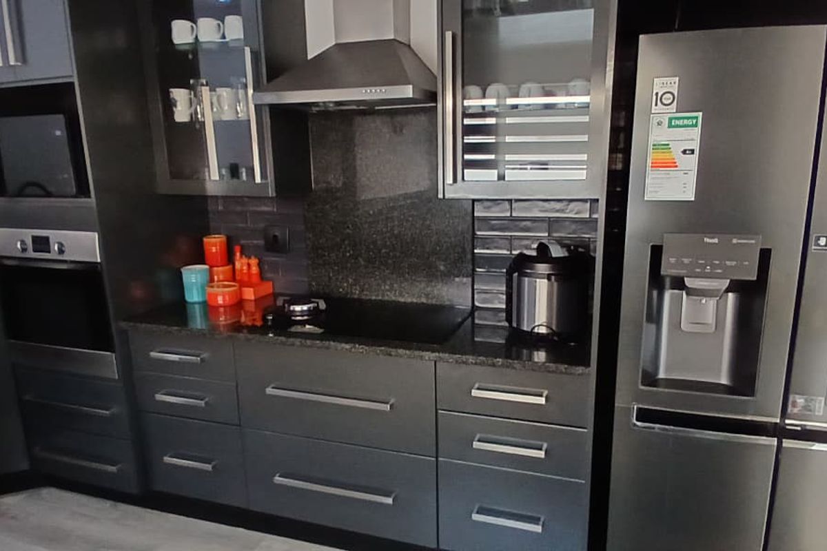 Modern kitchen featuring dark cabinetry, granite countertops, a built-in oven, microwave, and stainless steel extractor fan.