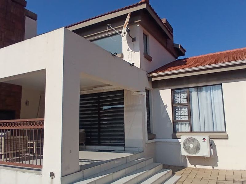 A rear exterior view of the house featuring a covered patio with a built-in fireplace, tiled steps, and an external air conditioning unit.