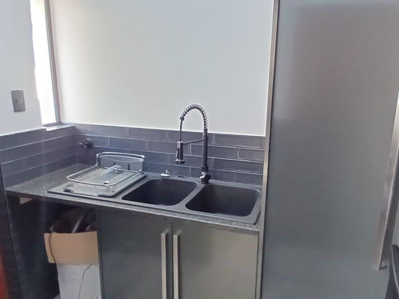 A functional scullery area featuring dark cabinetry, a double basin sink with a modern gooseneck faucet, and dark subway tile backsplash.