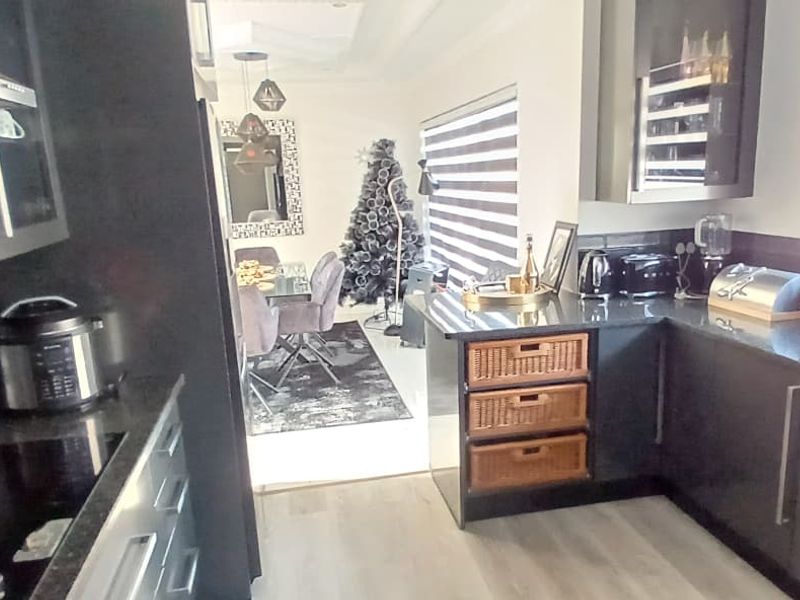 Modern open-plan kitchen featuring dark cabinetry, stone countertops, integrated hob, and extractor fan, flowing seamlessly into the adjacent dining area.