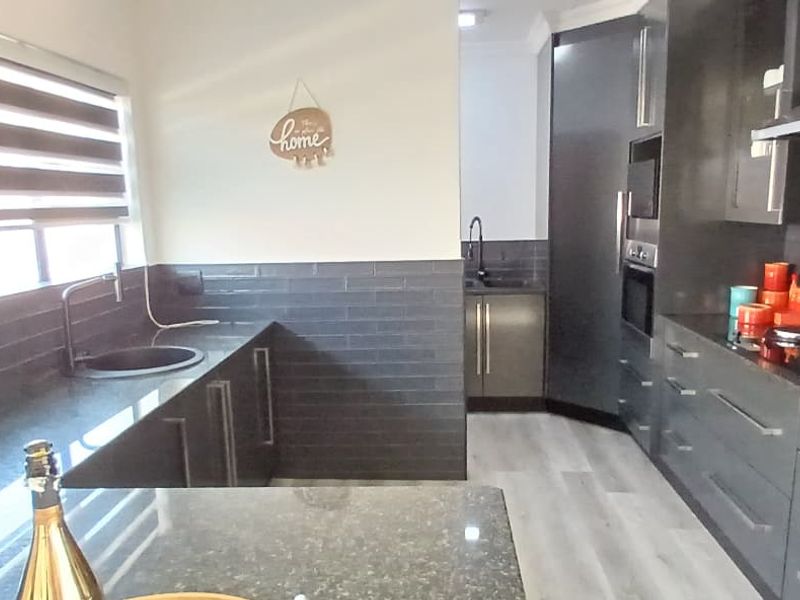 Modern kitchen featuring dark cabinetry, stone countertops, subway tile backsplash, integrated oven, and a secondary scullery area with additional sink.