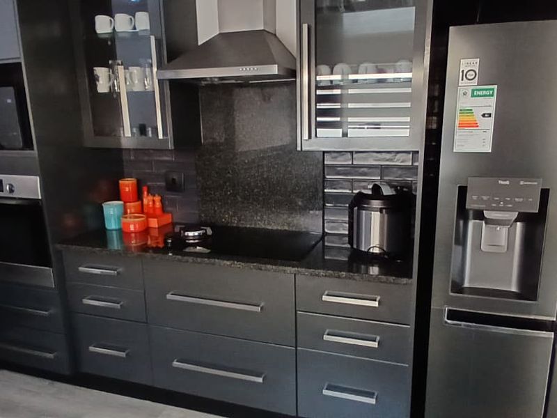 Modern kitchen featuring dark cabinetry, granite countertops, a built-in oven, microwave, and stainless steel extractor fan.