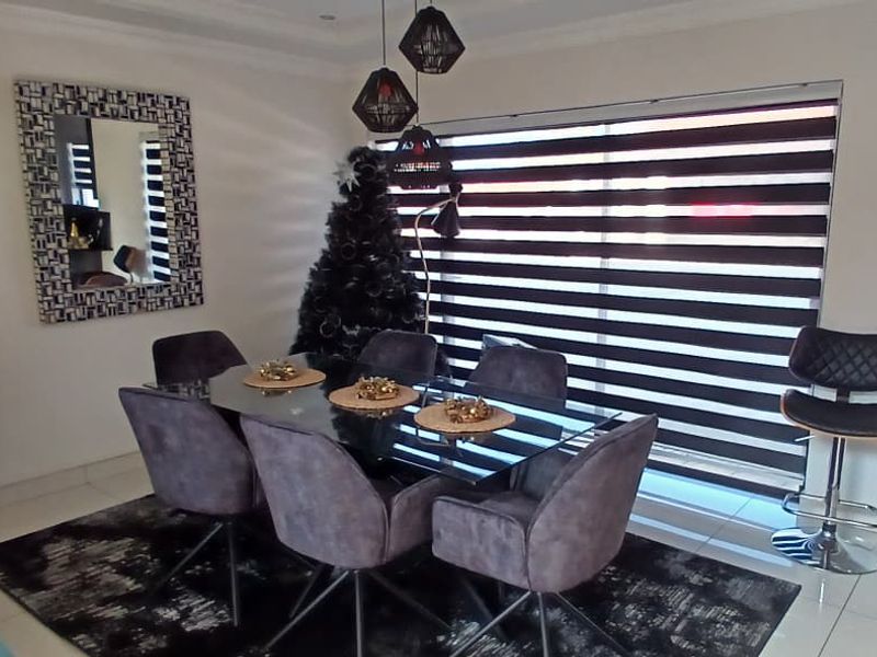 A well-maintained dining area featuring tiled flooring, modern pendant lighting, and large windows with fitted zebra blinds.