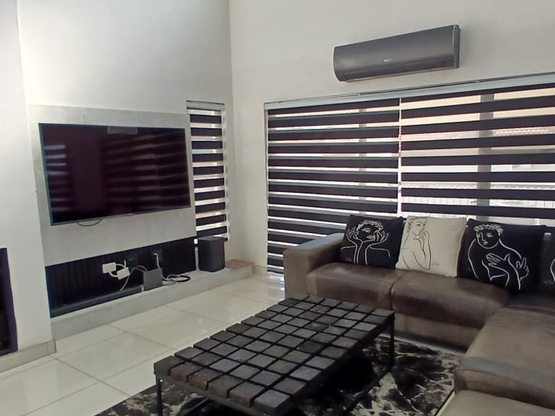 A modern living room featuring a built-in fireplace, tiled flooring, and large windows with fitted blinds, creating a bright and comfortable living space.