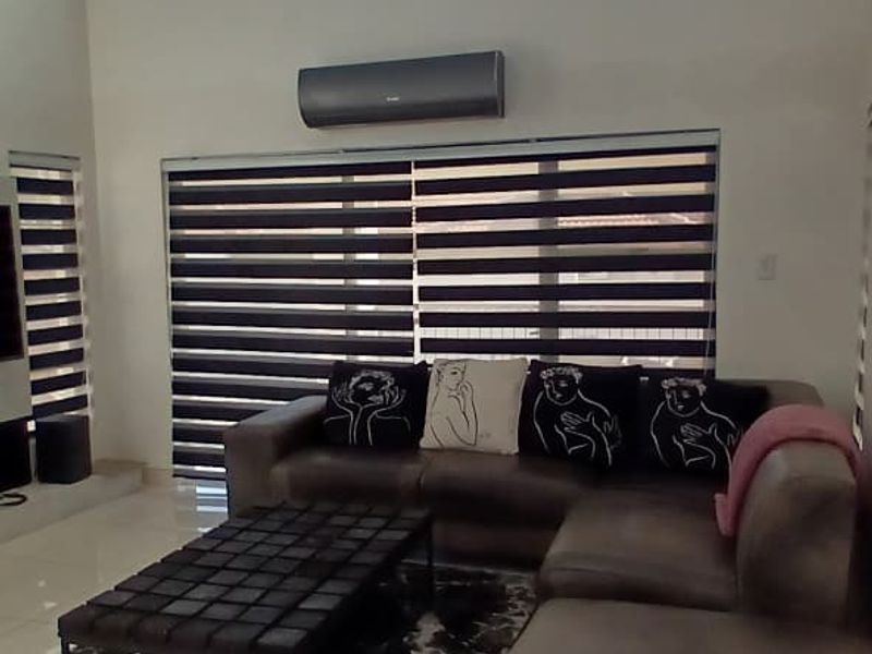 Spacious living room featuring high ceilings, large windows with modern zebra blinds, and a wall-mounted air conditioning unit.