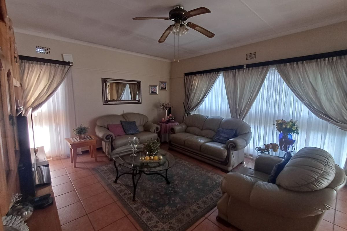 A spacious living room featuring tiled flooring, a ceiling fan, and large windows with curtains, providing a comfortable and functional living space.