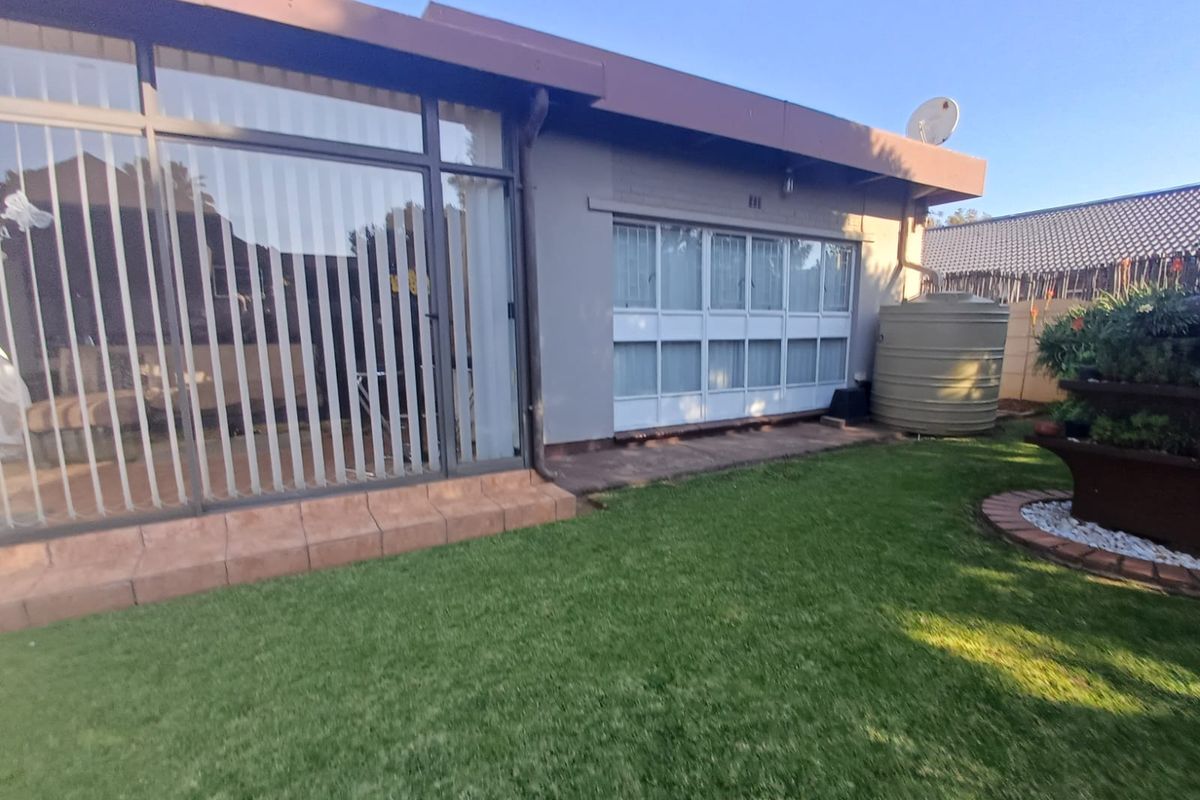 Rear view of the property featuring a paved patio area, large glass sliding doors, and a water storage tank set within a landscaped garden.