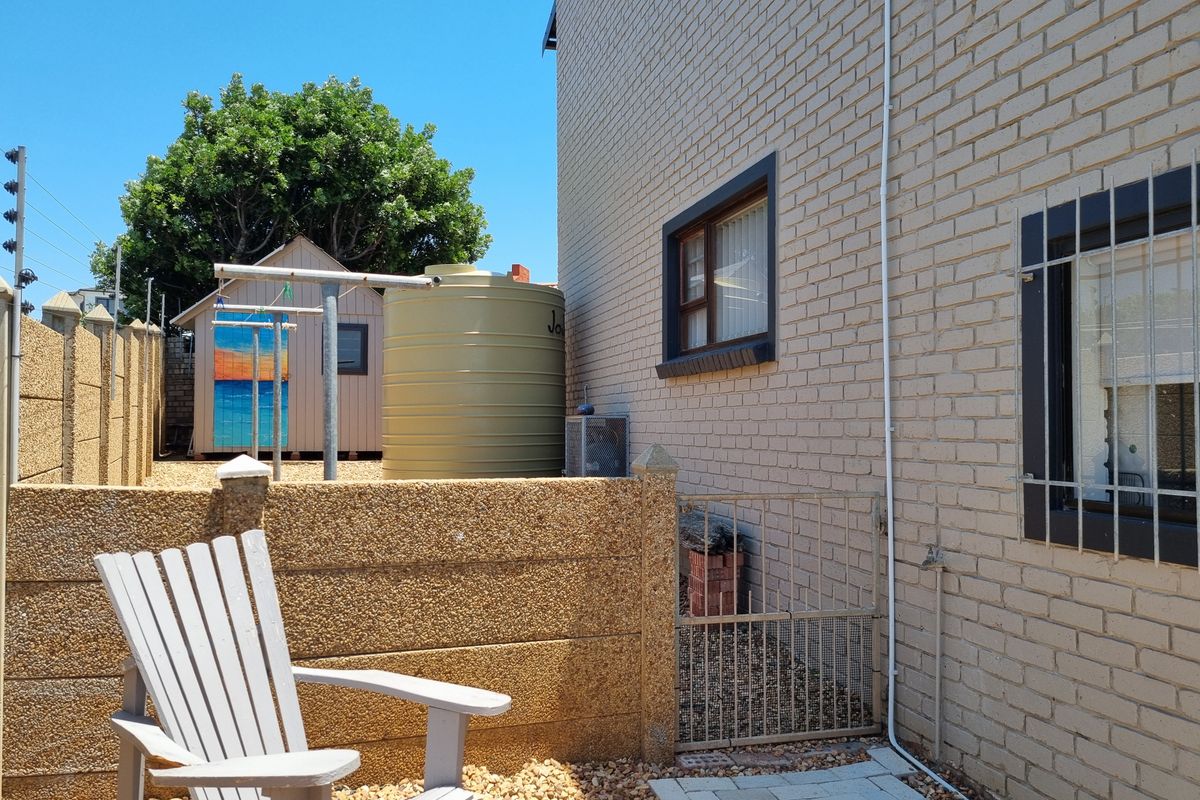 Side exterior view of the property featuring a brick facade, water tank, security gate, and perimeter electric fencing.