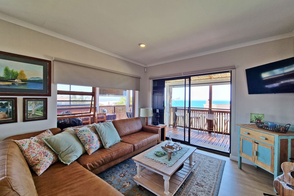 A bright living room featuring laminate flooring, recessed lighting, and large sliding glass doors that open onto a balcony with ocean views.