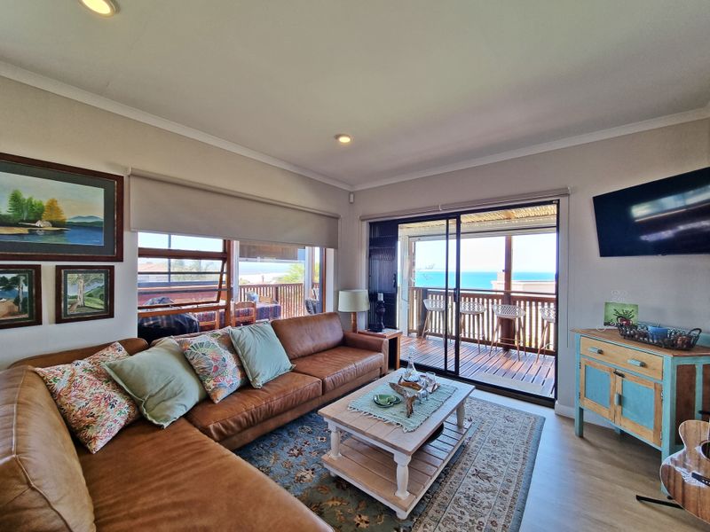 A bright living room featuring laminate flooring, recessed lighting, and large sliding glass doors that open onto a balcony with ocean views.