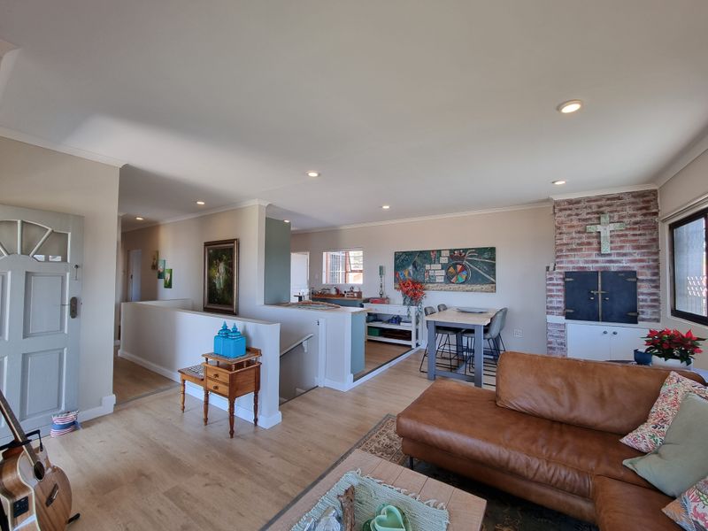 Spacious open-plan living area featuring laminate flooring, recessed lighting, and a characterful exposed brick fireplace, seamlessly connecting to the dining and stairwell zones.