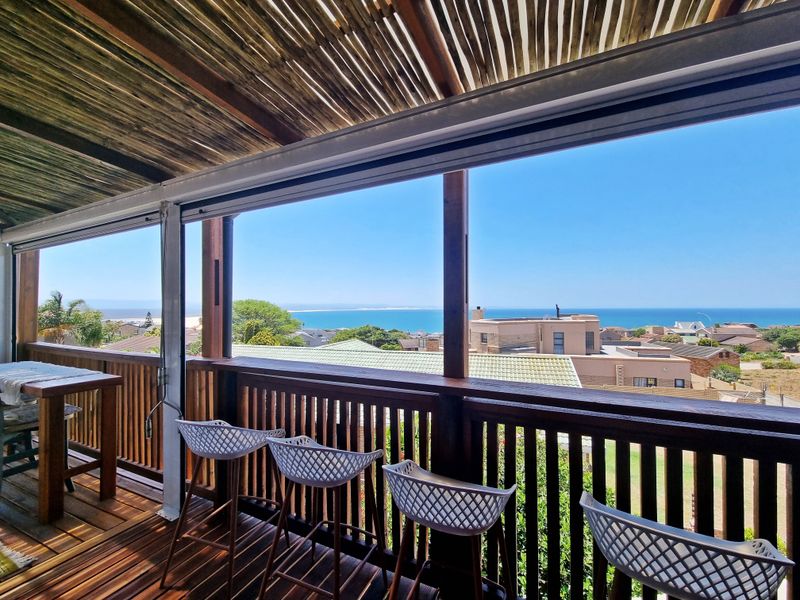 Covered timber balcony featuring a thatched roof and wooden balustrade, offering expansive coastal and ocean views.