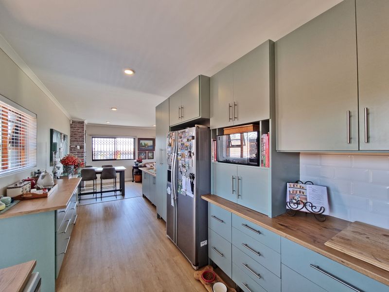 A modern open-plan kitchen featuring sage green cabinetry, timber countertops, and subway tile backsplash, flowing seamlessly into the adjacent dining and living area.
