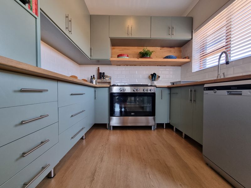 Modern kitchen featuring sage green cabinetry, wooden countertops, subway tile backsplash, and a stainless steel oven with integrated hob.