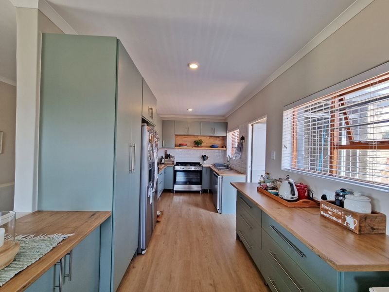 Modern galley-style kitchen featuring sage green cabinetry, warm wooden countertops, subway tile backsplash, and integrated stainless steel appliances.
