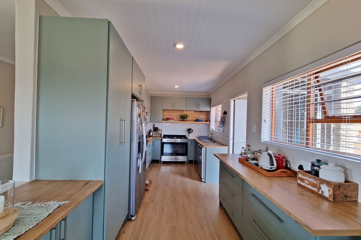 Modern galley-style kitchen featuring sage green cabinetry, warm wooden countertops, subway tile backsplash, and integrated stainless steel appliances.