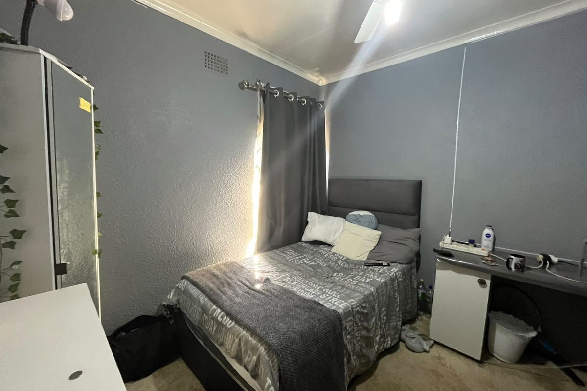 A compact bedroom featuring grey painted walls, a ceiling fan, and carpeted flooring.
