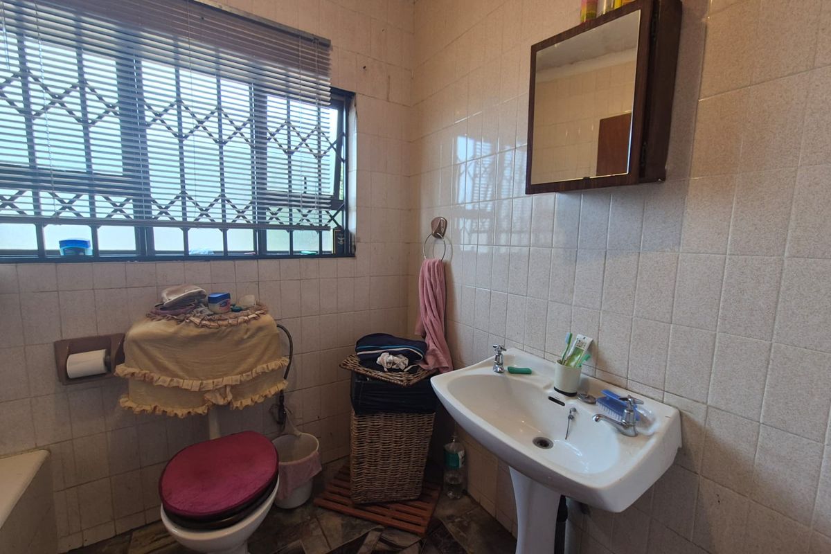 A dated bathroom featuring a pedestal sink, toilet, and full-height wall tiling, equipped with a security gate on the window.