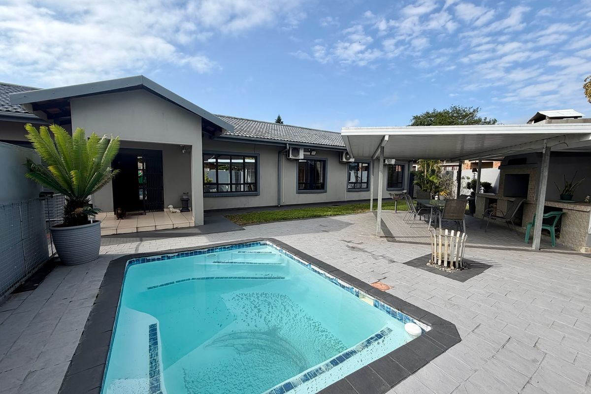 Spacious outdoor entertainment area featuring a swimming pool, paved patio, and a covered built-in braai area, perfect for relaxed outdoor living.