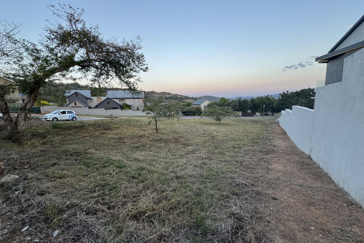 A vacant residential plot featuring a gentle slope, established boundary wall, and surrounding neighborhood views.