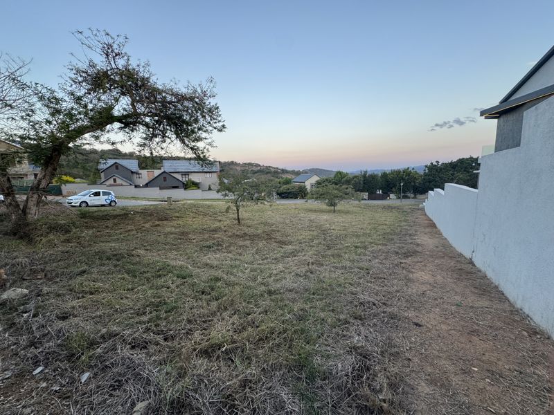 A vacant residential plot featuring a gentle slope, established boundary wall, and surrounding neighborhood views.