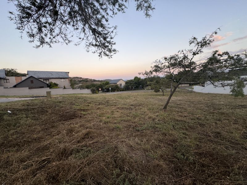 A view of a vacant residential plot of land with surrounding neighborhood houses visible in the background.
