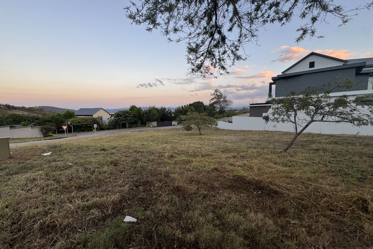 A vacant residential plot situated in a developed estate, featuring natural grass cover and adjacent boundary walling.