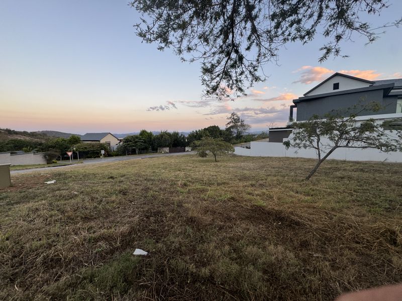 A vacant residential plot situated in a developed estate, featuring natural grass cover and adjacent boundary walling.