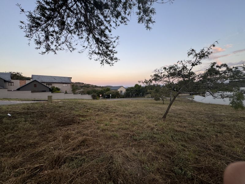 A view of a vacant residential plot of land with surrounding neighborhood houses visible in the background.
