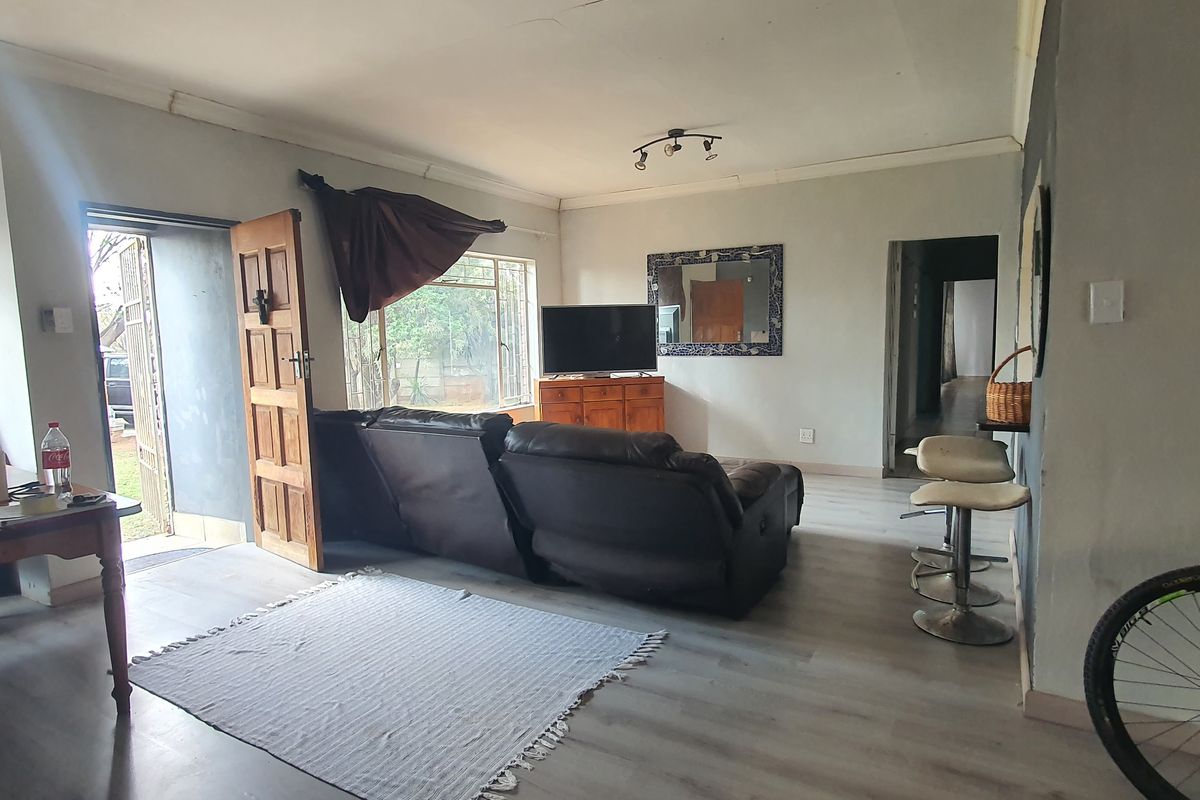 A living room featuring laminate flooring and access to the exterior, showing signs of wear on the walls and ceiling.