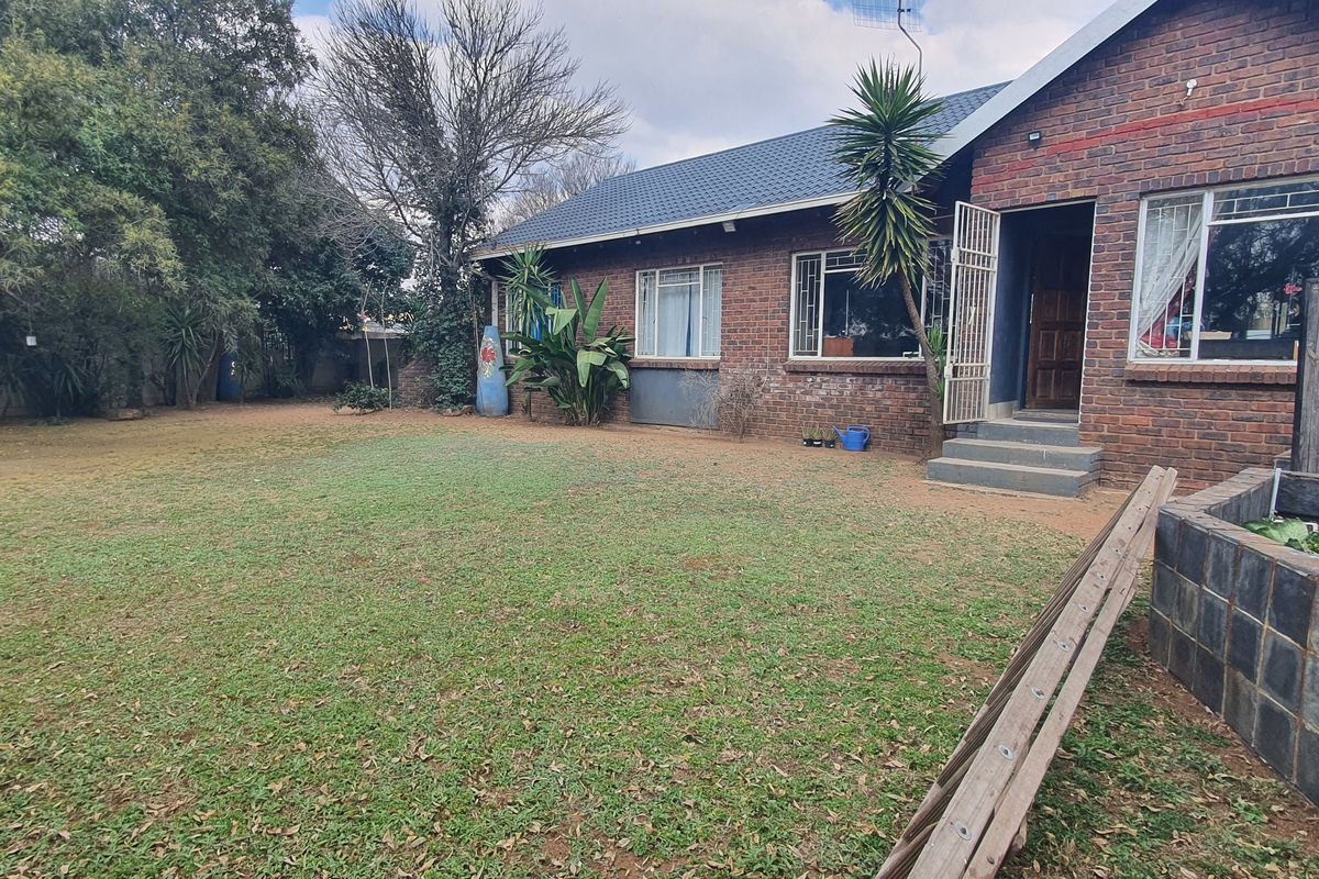 A rear view of a brick-faced house featuring a spacious garden, concrete entrance steps, and a stone-clad planter box.