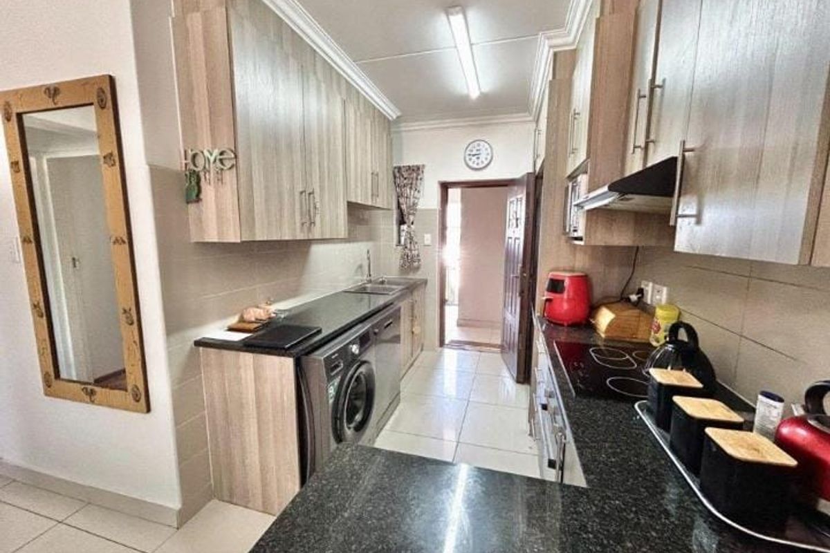 A functional galley-style kitchen featuring laminate cabinetry, granite countertops, integrated appliances, and tiled flooring with a direct access point to the hallway.