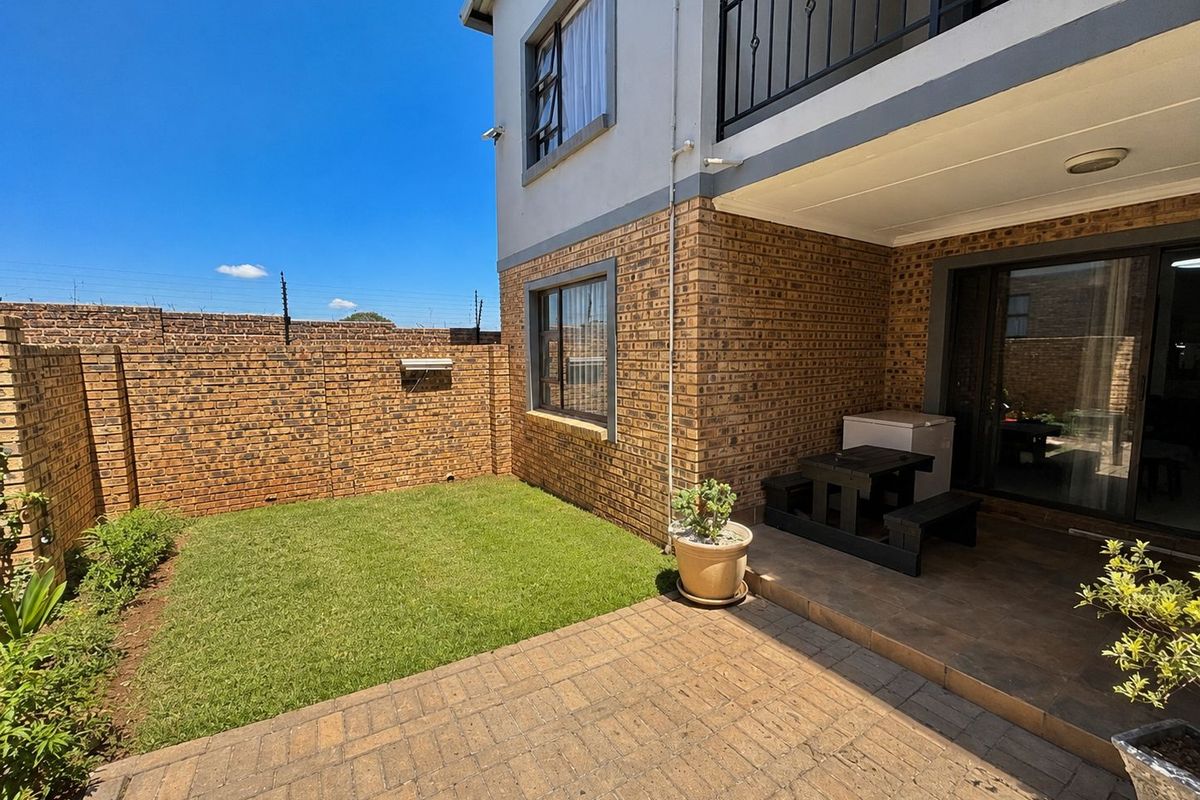 A private rear garden featuring a paved patio area, a small lawn, and a brick boundary wall, with access to the apartment via sliding doors.