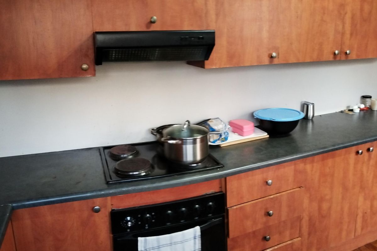A functional kitchen featuring wood-veneer cabinetry, a built-in oven, electric hob, and an extractor fan with dark laminate countertops.