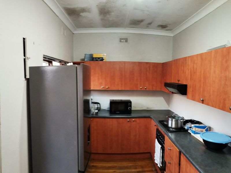 A compact kitchen featuring wooden cabinetry, dark countertops, and integrated cooking appliances, requiring maintenance to the ceiling.