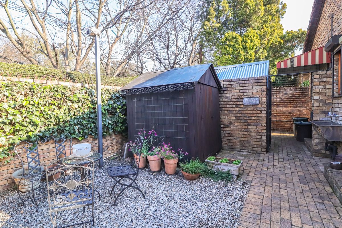 A private rear courtyard featuring brick boundary walls, paved pathways, a gravel seating area, and a built-in utility sink.