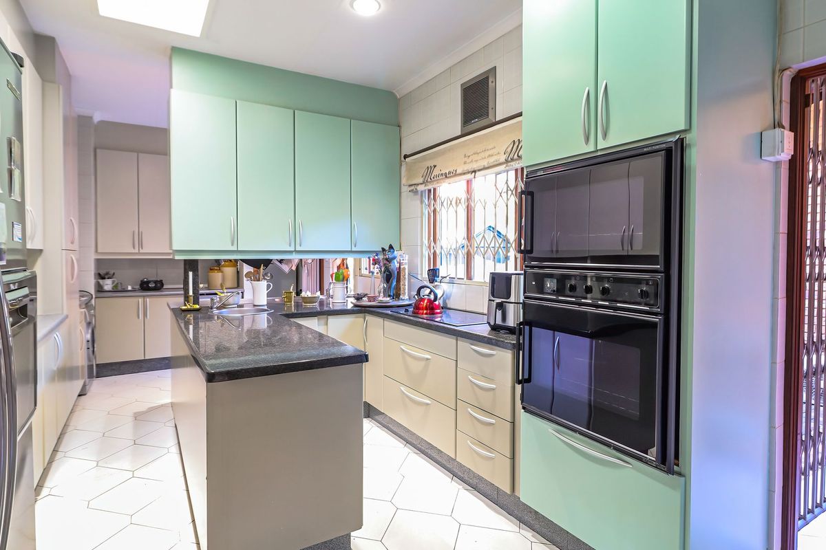 A functional kitchen featuring mint green cabinetry, dark granite countertops, a built-in double oven, and tiled flooring with a breakfast bar layout.