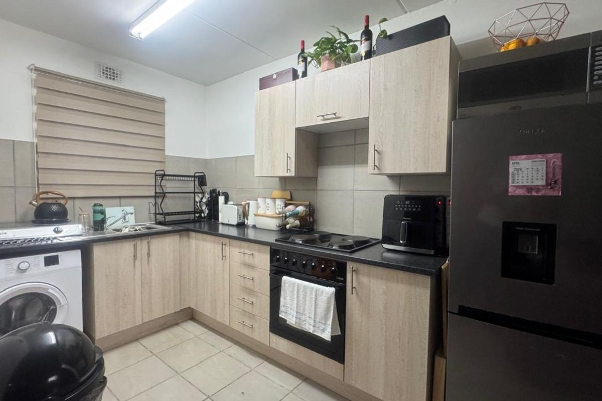 Functional kitchen featuring light wood-grain cabinetry, dark countertops, integrated oven and hob, and a dedicated space for a washing machine.