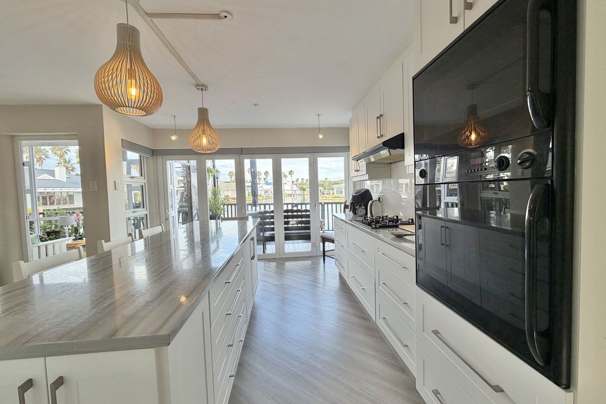Modern kitchen featuring a large island with stone countertops, built-in oven, gas hob, and shaker-style cabinetry, opening directly onto an outdoor patio area.